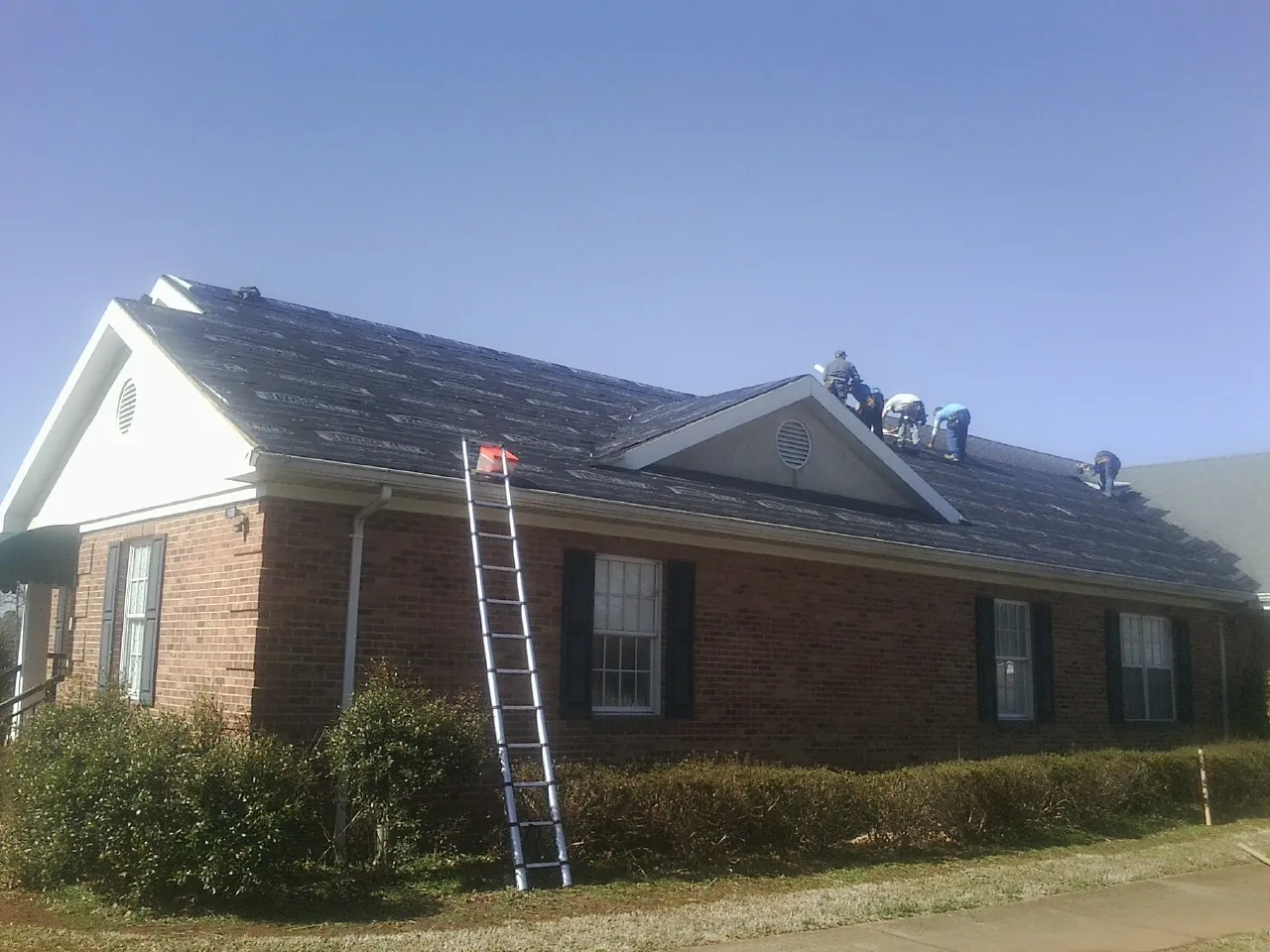 Crew tearing shingles off a brick ranch roof with a ladder set — Emergency Roof Repair work by our crew in Wilton